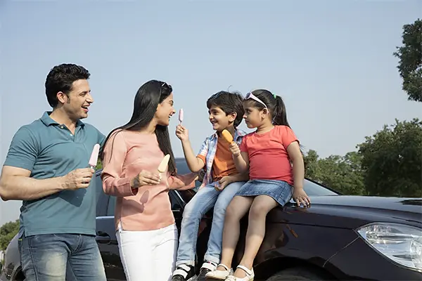happy family enjoying ice creams together outdoors with two children sitting on a car and parents standing nearby sharing a joyful moment